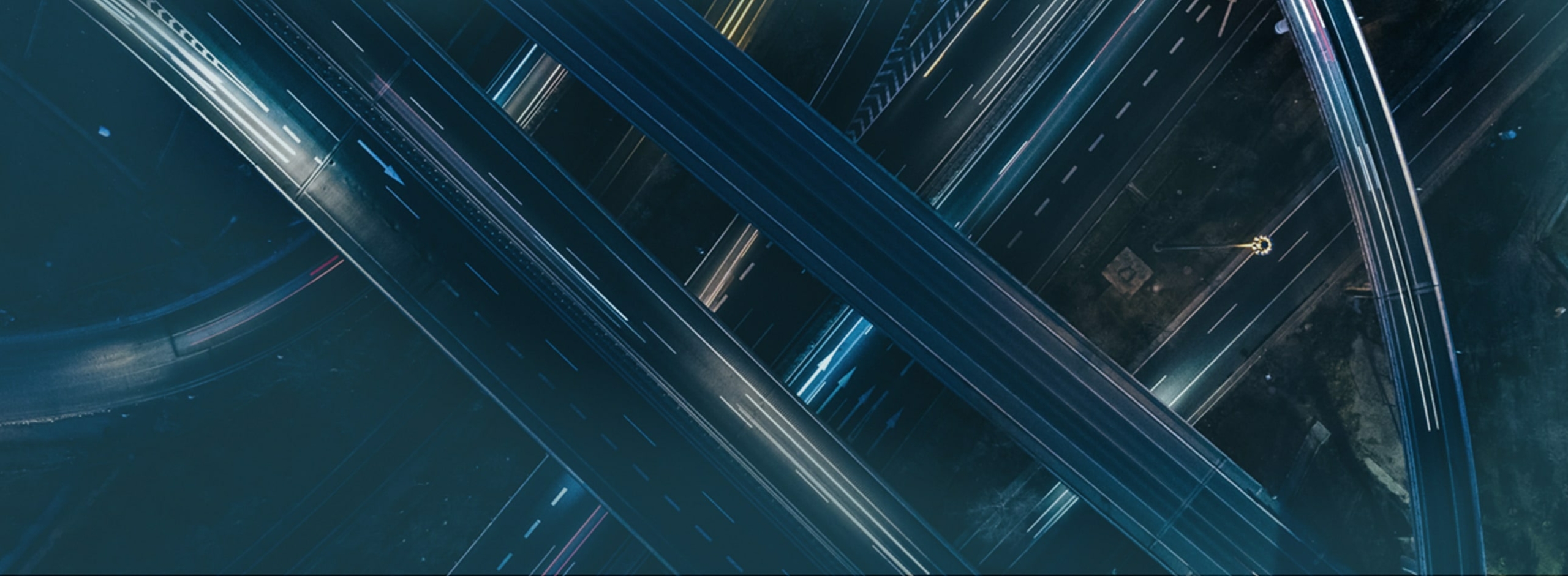 Aerial view of a complex, multi-level highway interchange at night with light trails from moving vehicles.