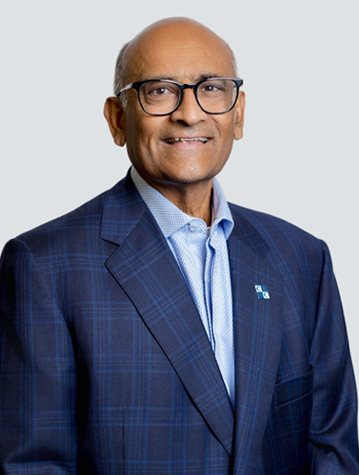 A man in a plaid suit jacket and blue shirt smiles at the camera against a plain background.