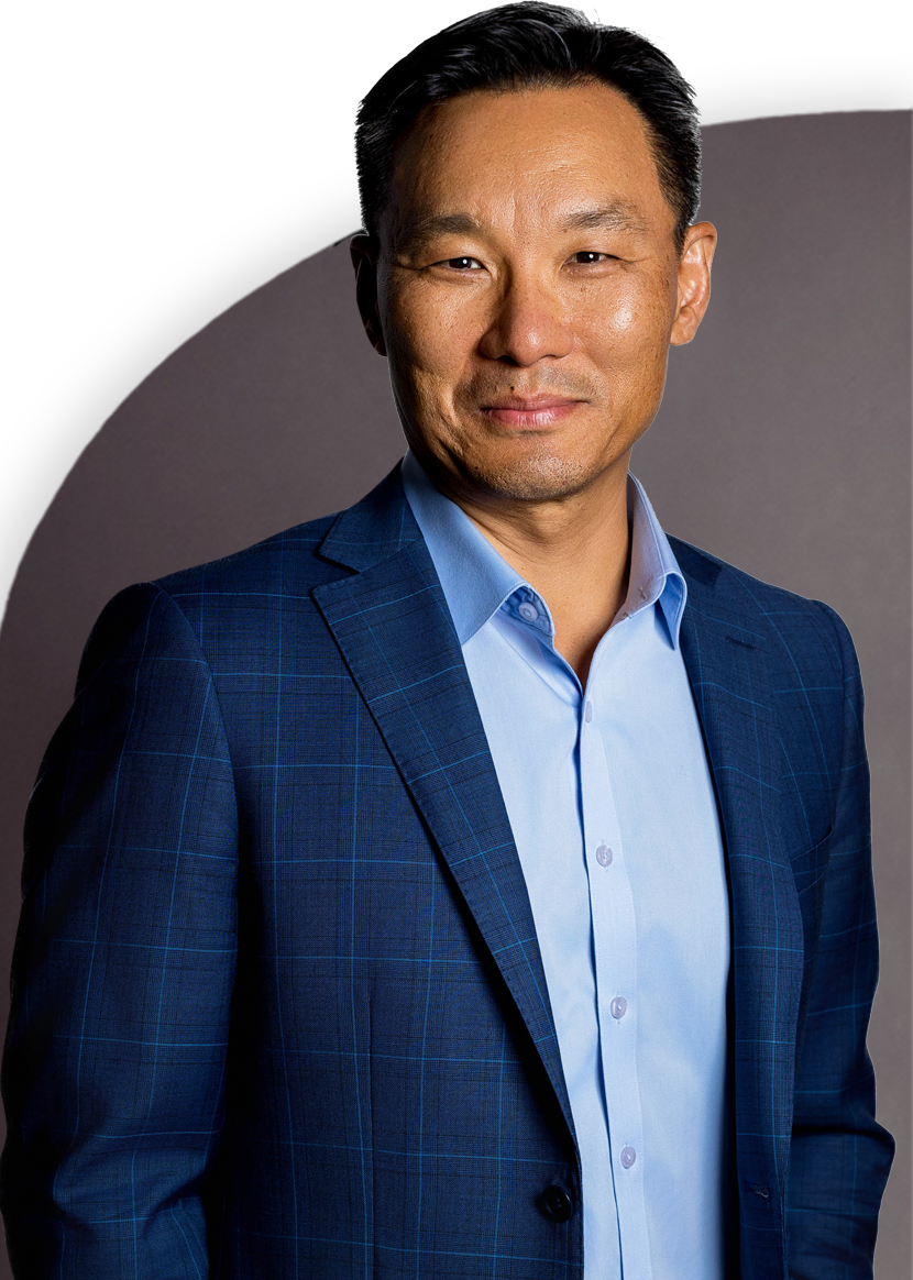 A person in a blue suit and light blue shirt smiles, standing against a plain background.