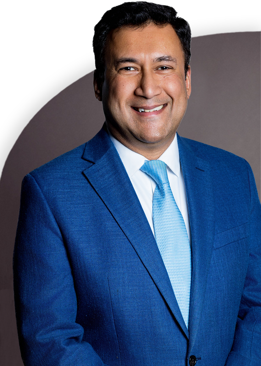 Smiling man in a blue suit and light blue tie against a dark background.