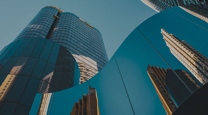 Modern skyscrapers with glass exteriors reflecting other buildings against a clear blue sky.