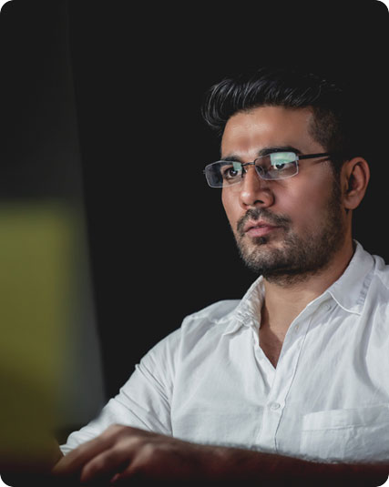 A man wearing glasses and a white shirt is intently looking at a computer screen.