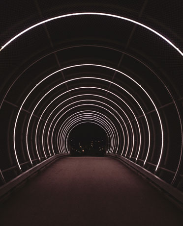 A dark tunnel with concentric circles of white neon lights lining the interior, creating a glowing passage.