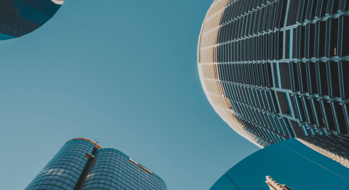 Low-angle view of modern skyscrapers with glass and steel facades against a clear blue sky, showcasing contemporary urban architecture.