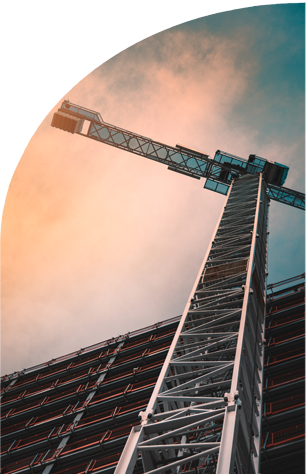 A construction crane extends high above a building frame against a cloud-filled sky with a gradient of sunset colors.