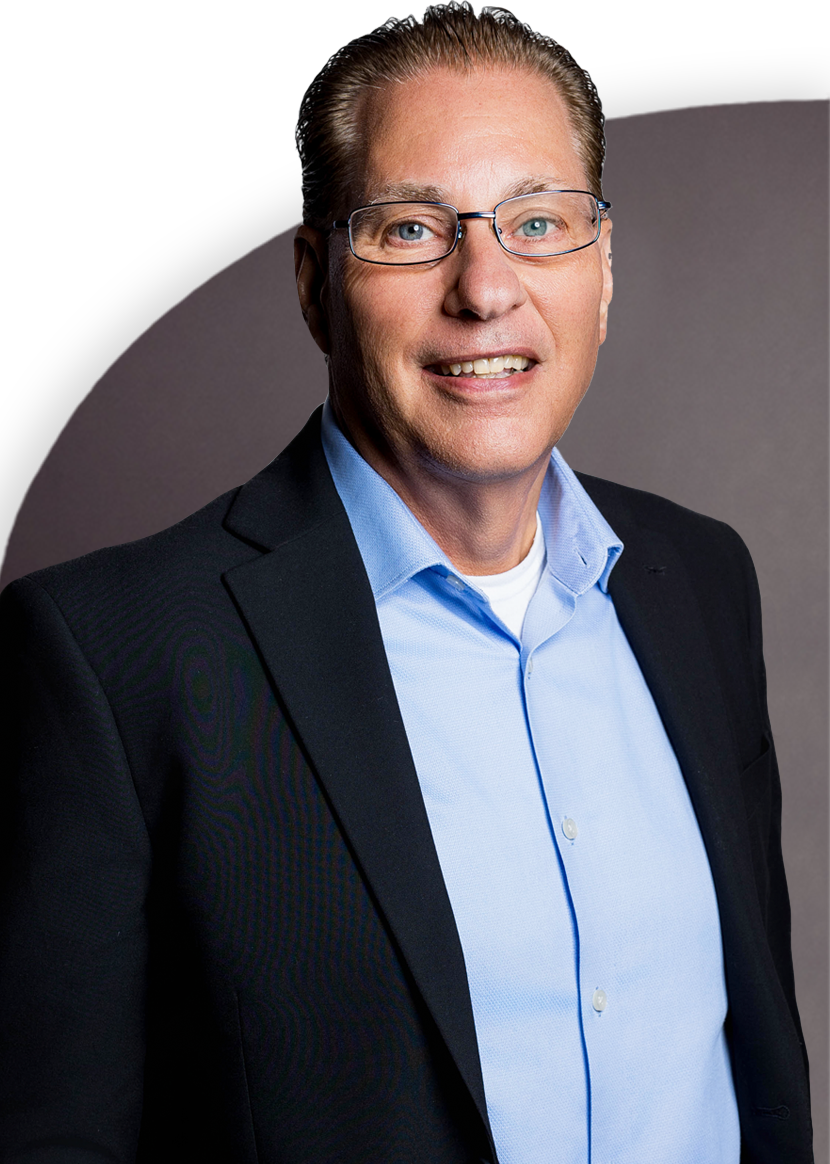 Man in glasses wearing a blue shirt and dark blazer, smiling against a plain background.