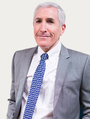 A man in a gray suit with a blue patterned tie stands against a plain background.