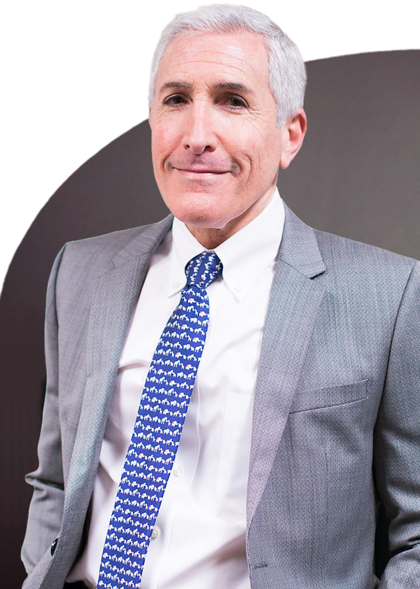 A man with short gray hair in a gray suit, white shirt, and patterned blue tie stands against a dark background, smiling slightly.