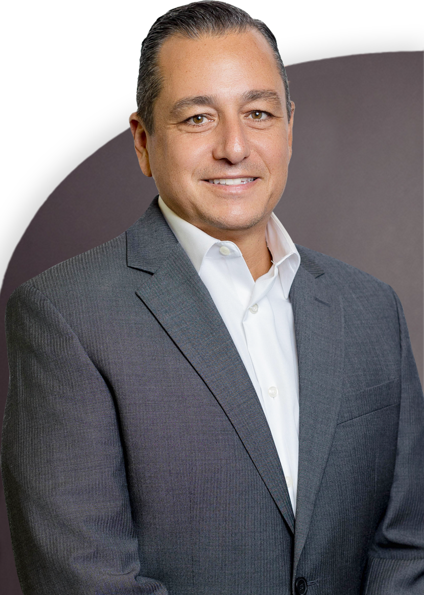 A man in a grey suit and white shirt is smiling against a dark background.