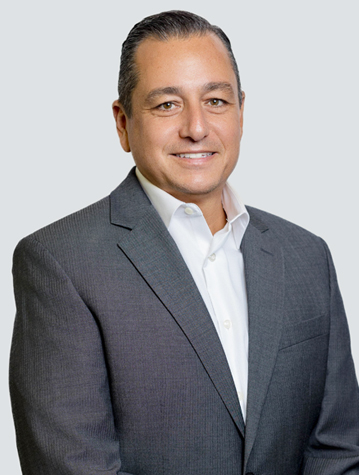 Smiling man in a gray suit and white shirt against a light background.