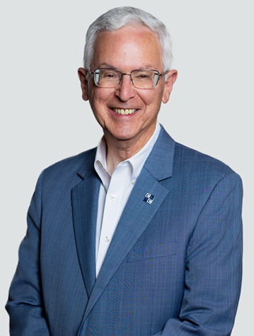 A man in a blue suit and white shirt smiles at the camera against a plain background.