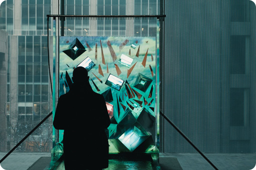 Silhouette of a person standing in front of a colorful, abstract glass art installation with a cityscape visible through a window in the background.