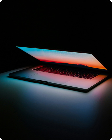 Partially open laptop on a dark surface, screen displaying colorful gradient light emitting a soft glow.