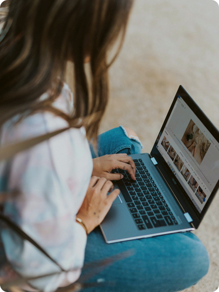 Person typing on a laptop while seated outdoors. The screen displays a website with images and text.