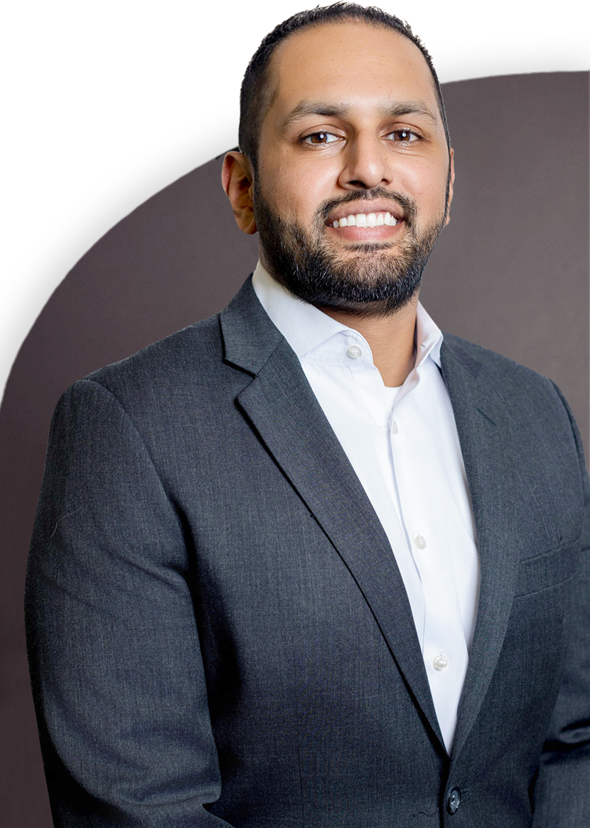 A person wearing a dark suit and a white shirt smiles at the camera against a plain background.