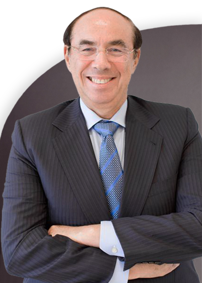 A man in a suit and striped tie stands with his arms crossed, smiling at the camera. He has short hair and glasses.