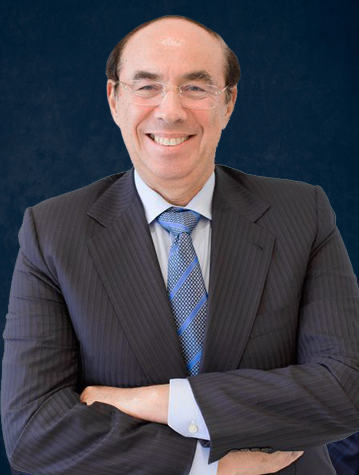 Smiling man with glasses in a dark pinstripe suit and blue tie, arms crossed in front of a dark blue background.