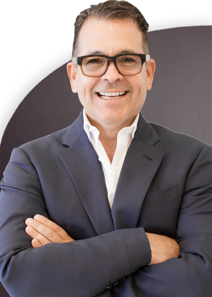 A person wearing glasses, a dark blazer, and a white shirt is seen smiling with arms crossed against a dark background.