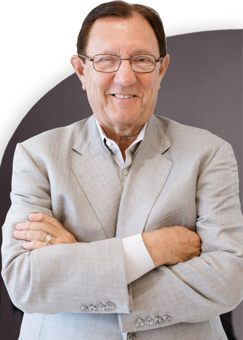 A man in a light gray suit and glasses stands with crossed arms, smiling at the camera.