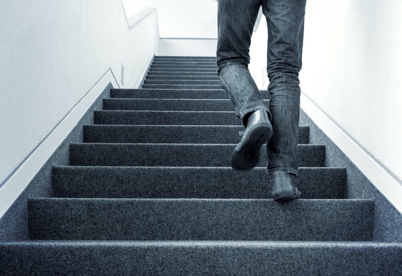 A person wearing jeans and black shoes is walking up a carpeted staircase.