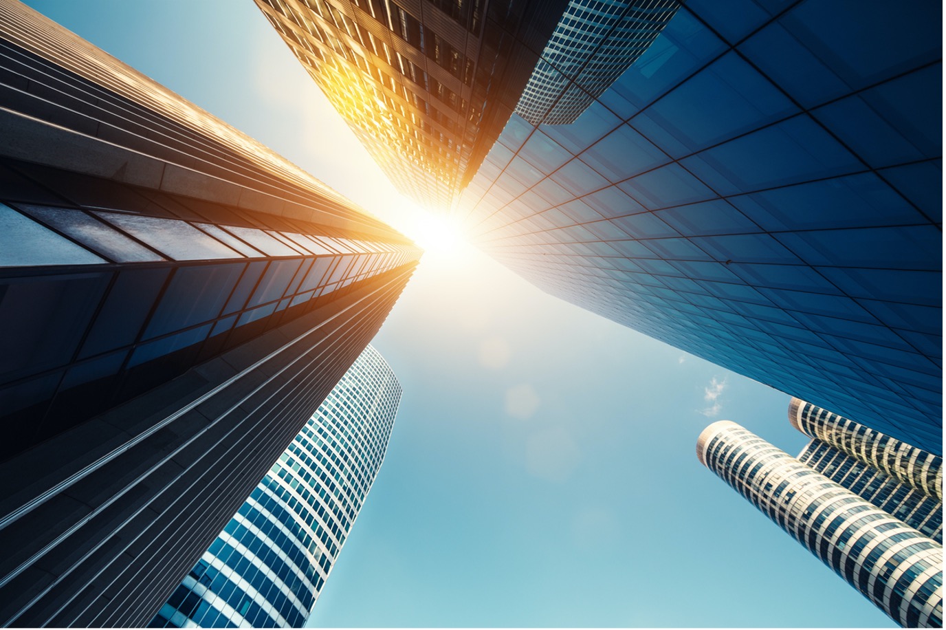 Upward view of modern skyscrapers reflecting sunlight, with a clear blue sky in the background.