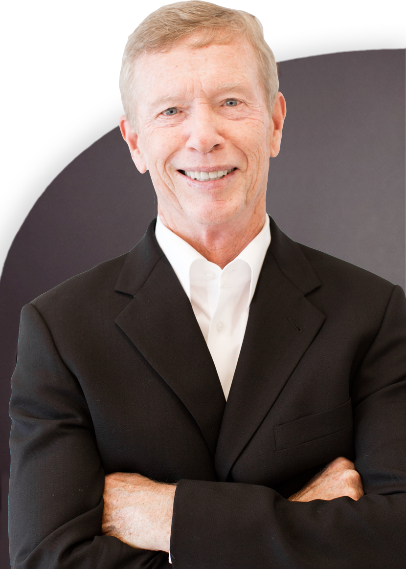 A man in a black suit jacket and white shirt stands with his arms crossed, smiling at the camera.