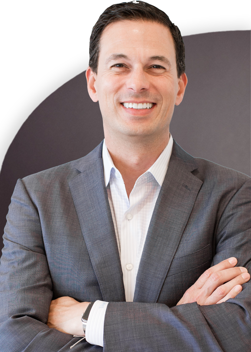 A man in a grey suit with a white shirt stands with arms crossed, smiling at the camera.