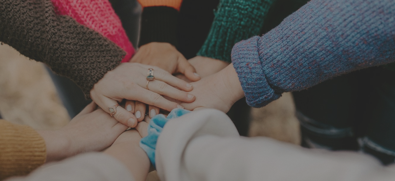 A group of people place their hands together in a circle, showcasing a sense of unity and teamwork.