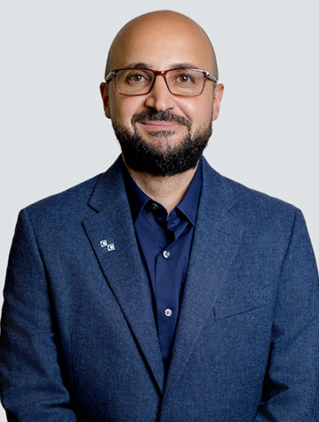 A man with a beard and glasses wearing a blue blazer and shirt stands against a light background.