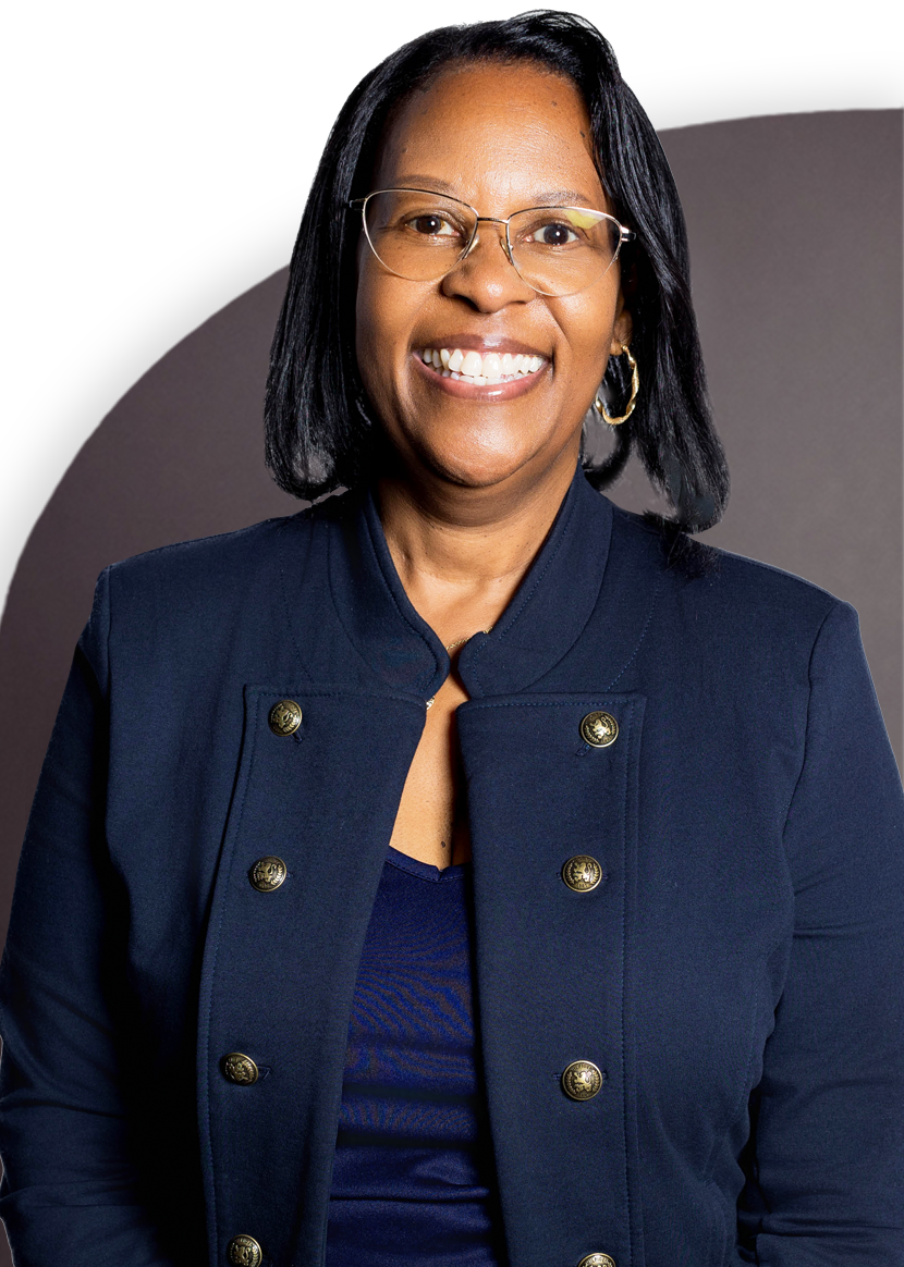 A person wearing glasses and a dark jacket, smiling at the camera with a neutral background.