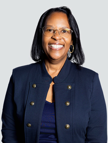 Smiling person wearing glasses and a dark blazer against a plain background.