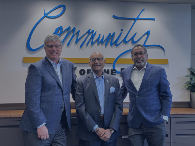 Three men in suits stand smiling in front of a sign that reads "Community.