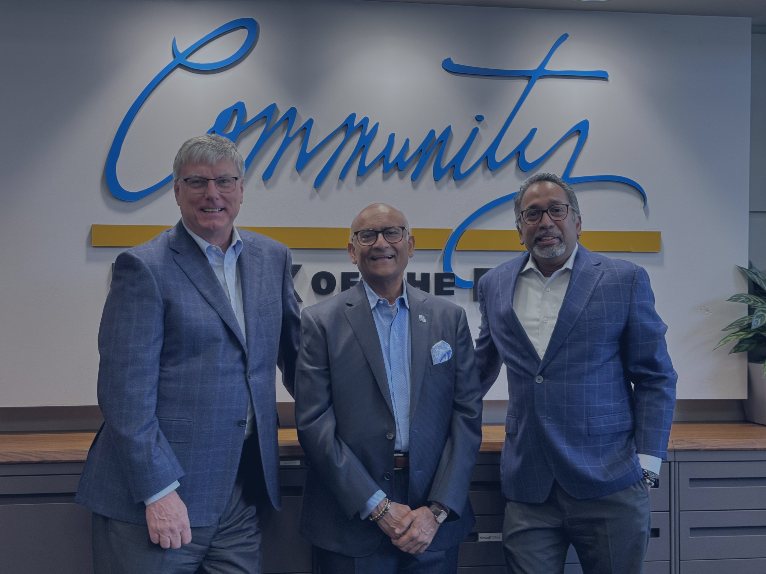 Three men in suits stand smiling in front of a sign that reads "Community.