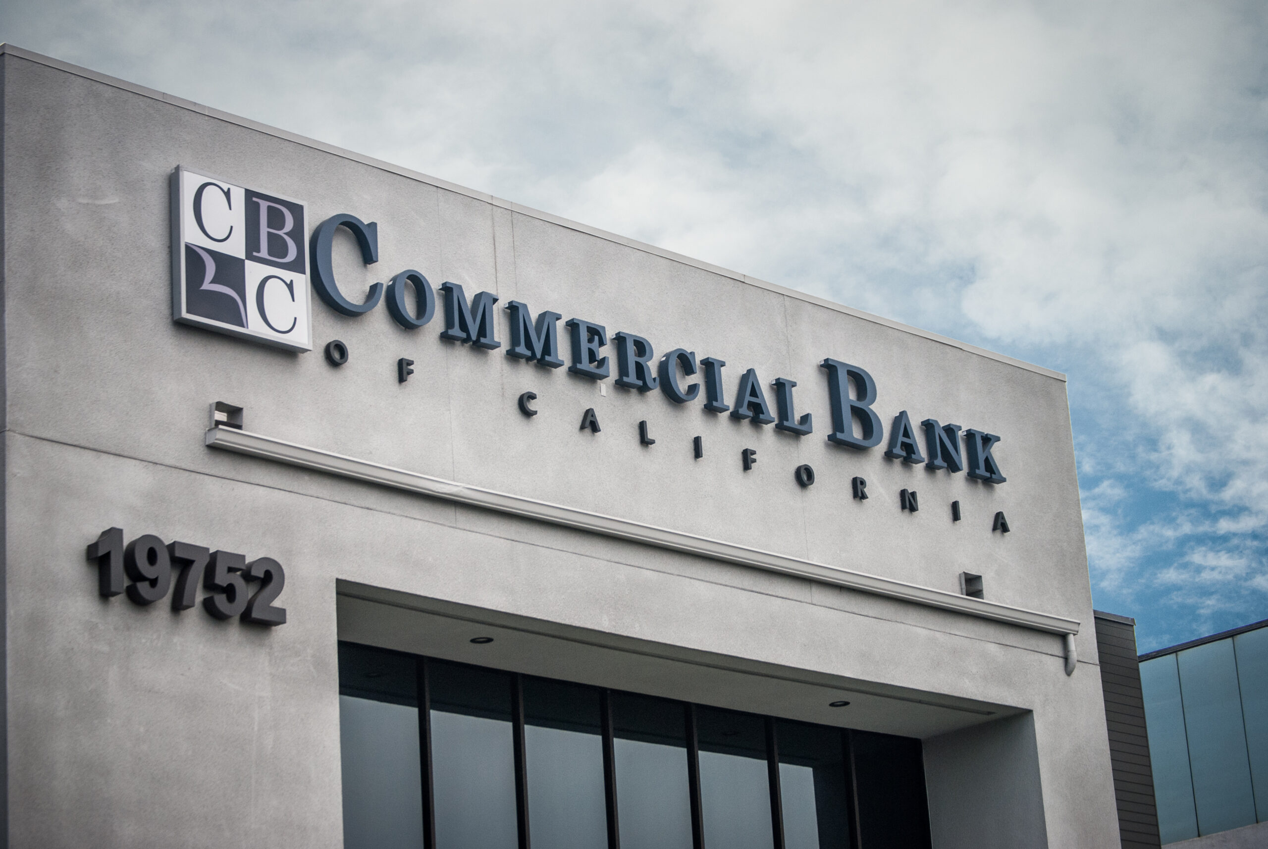 Exterior of Commercial Bank of California building with its logo and address number 19752 displayed on a gray facade.