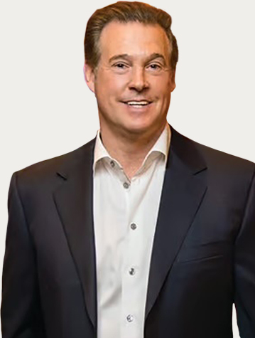 A man in a dark suit jacket and white shirt is smiling at the camera.