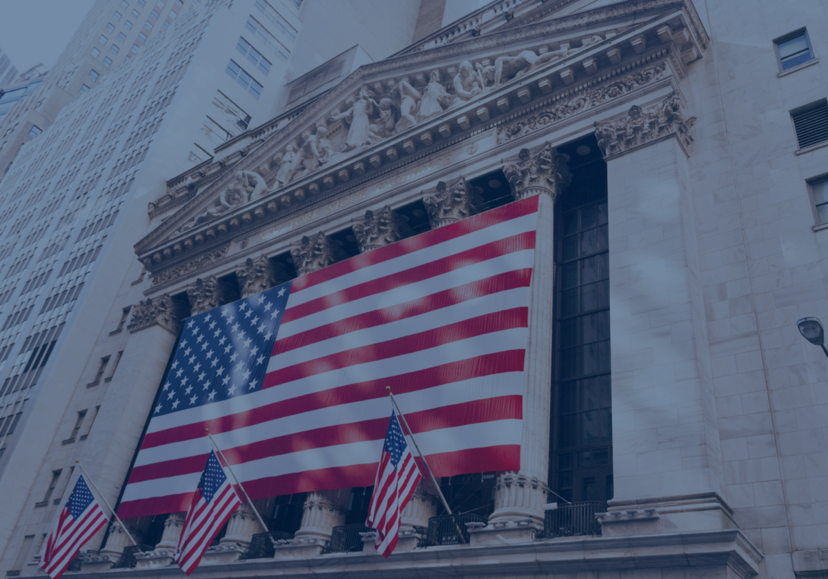 The building facade, adorned with a large American flag and flanked by columns and ornate sculptures, stands proudly amidst towering skyscrapers. Smaller flags flutter below, reminiscent of steady interest rates that anchor the bustling city's economic landscape.